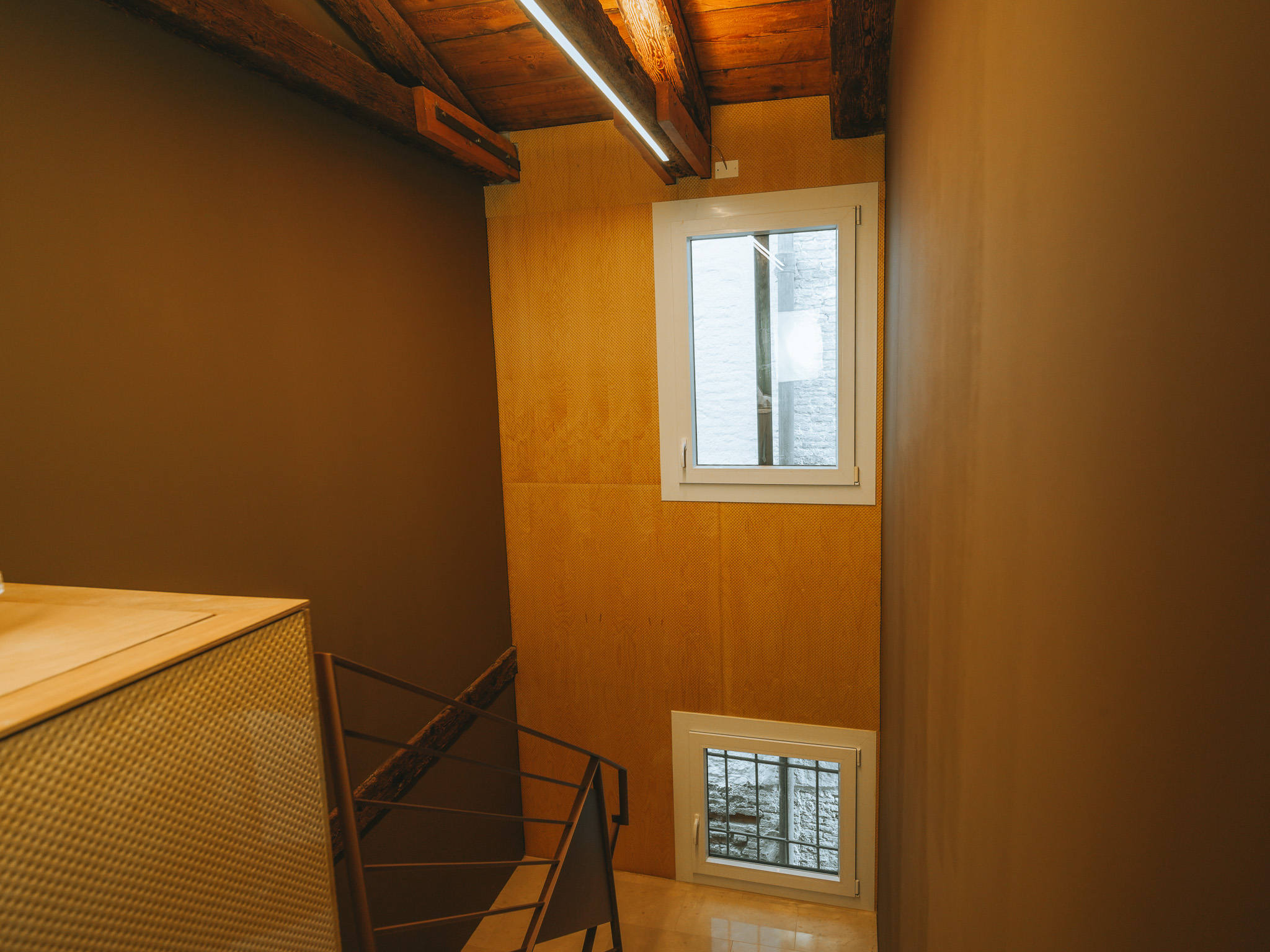 Landing with exposed wooden beams, two windows and a staircase with a metal railing.