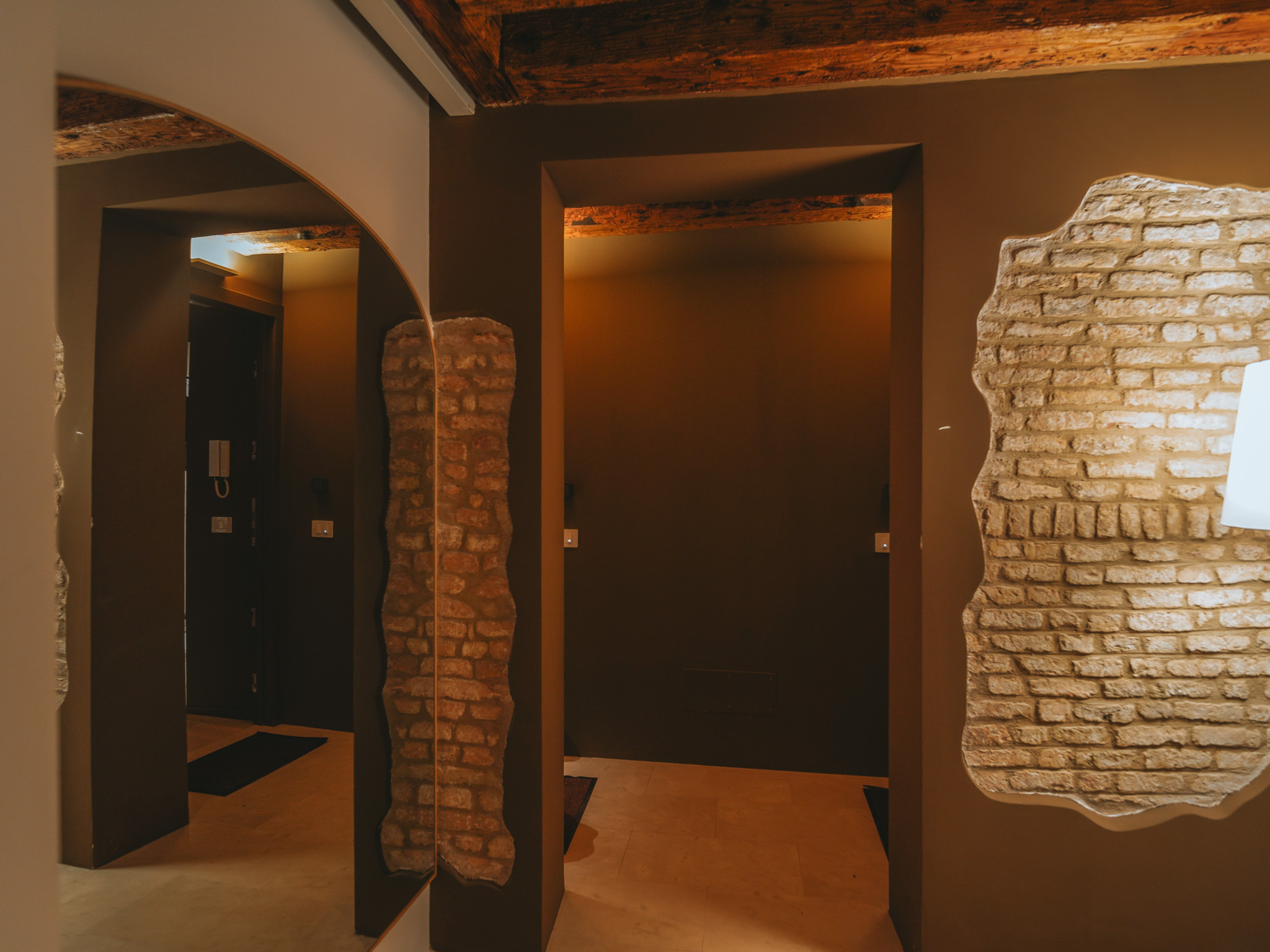 Hallway with patches of exposed brickwork, an arched mirror and wooden ceiling beams.