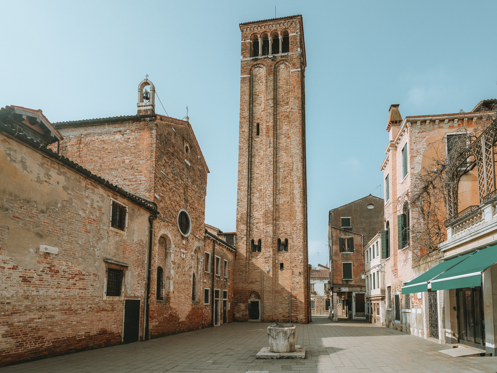 Paved square with a brick church, a tall bell tower and a stone wellhead at the centre.